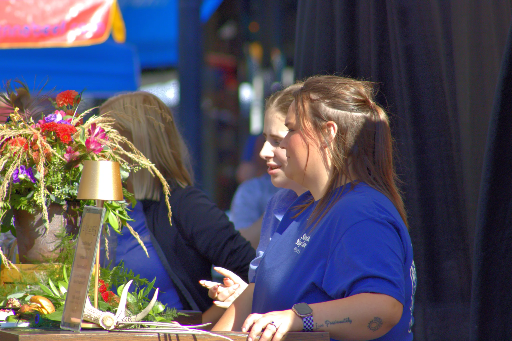 Two people talking beside flowers at an outdoor booth at Baraboo's 2026 Fall Fair on the Square
