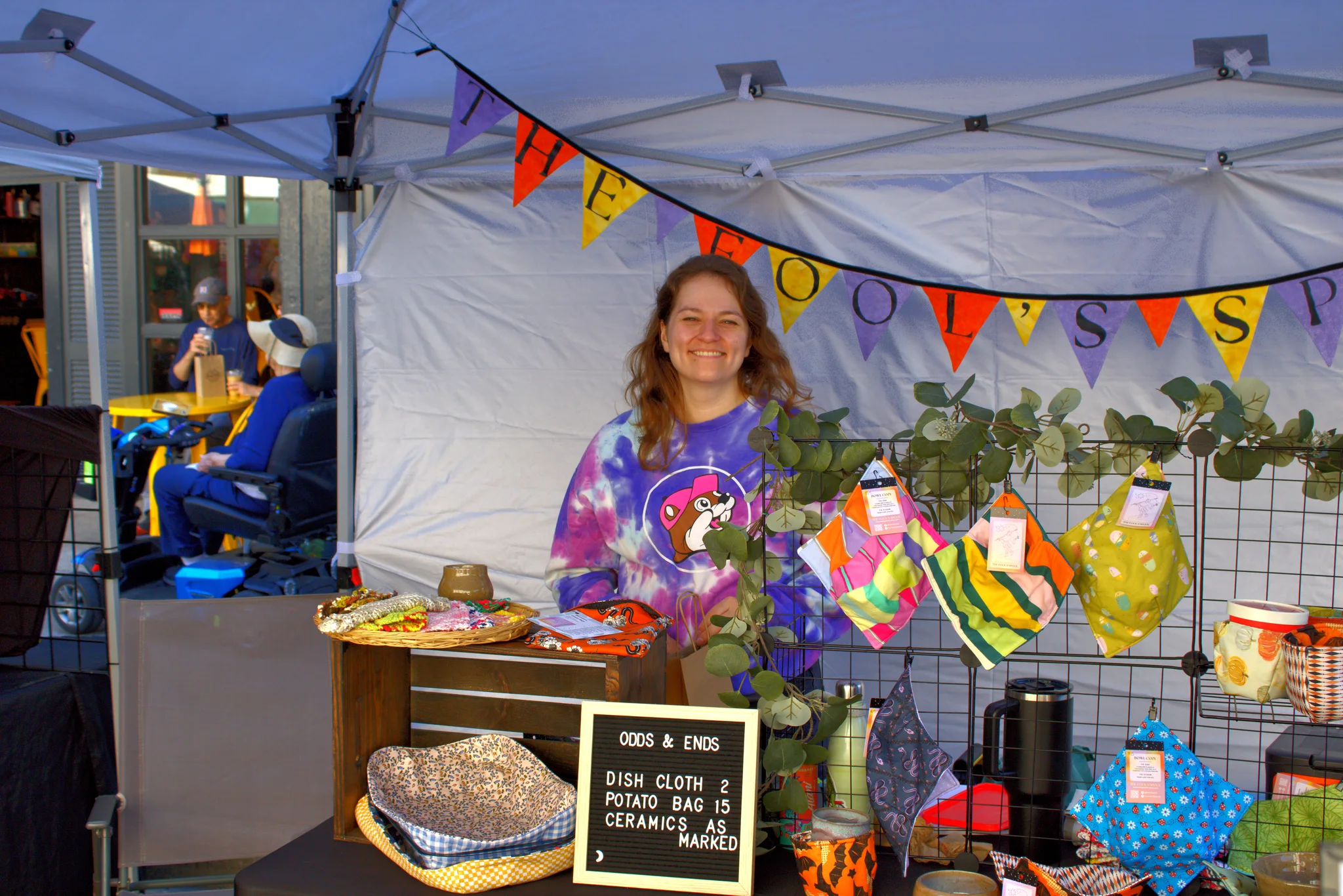 Smiling maker behind a colorful handmade-goods display at Baraboo's 2026 Fall Fair on the Square