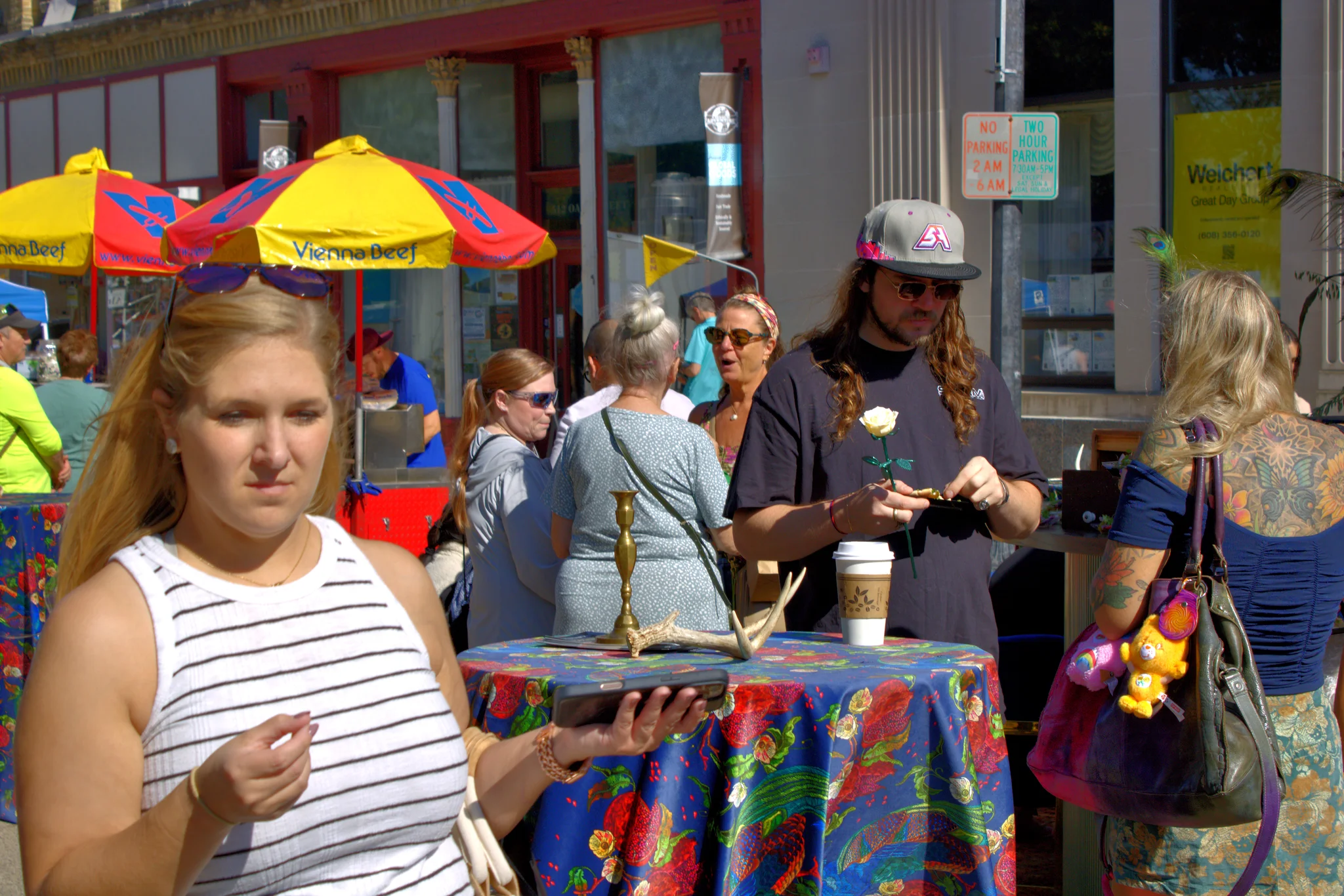 Visitor carrying food past a colorful downtown stand at Baraboo's 2026 Fall Fair on the Square