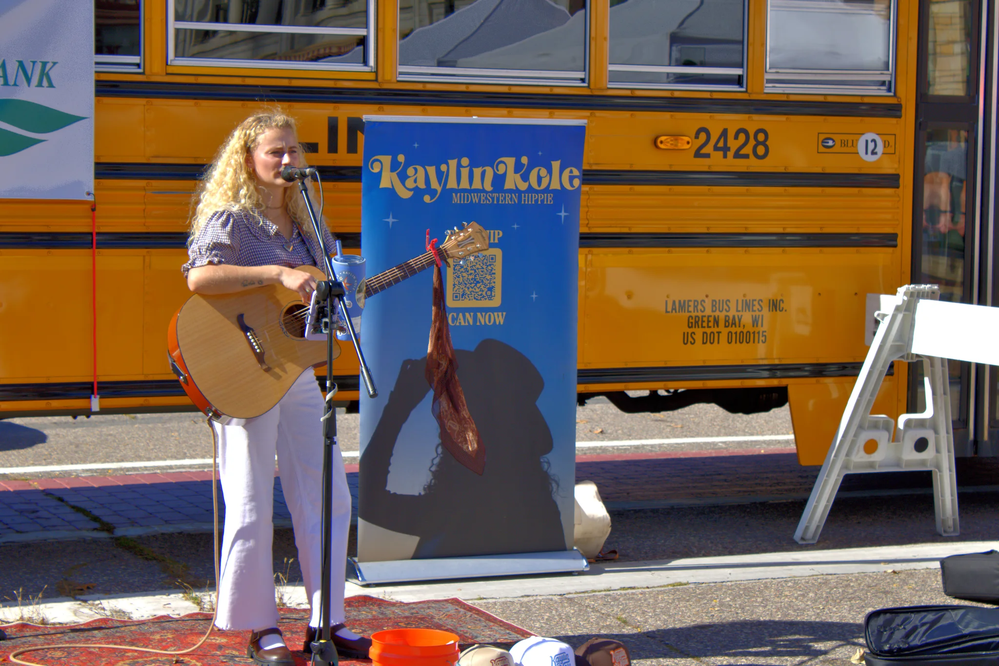 Musician performing with a guitar beside a yellow school bus at Baraboo's 2026 Fall Fair on the Square