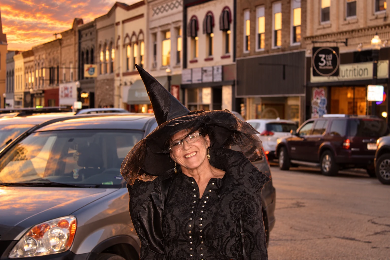 A smiling visitor wearing a broad witch hat and patterned black costume
