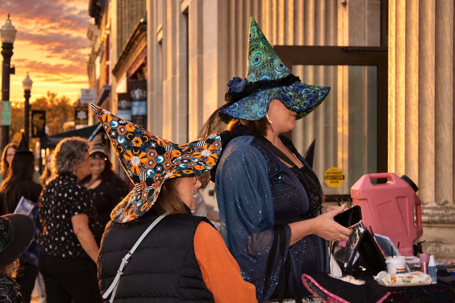 Visitors wearing peacock-patterned and orange printed witch hats at an outdoor table