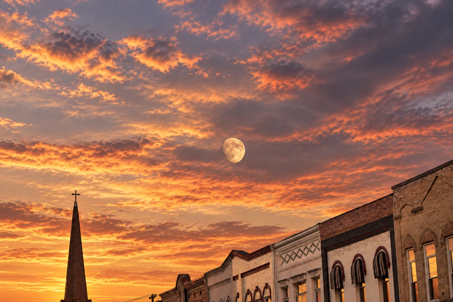 Downtown Baraboo storefronts and a church steeple beneath a warmly colored evening sky