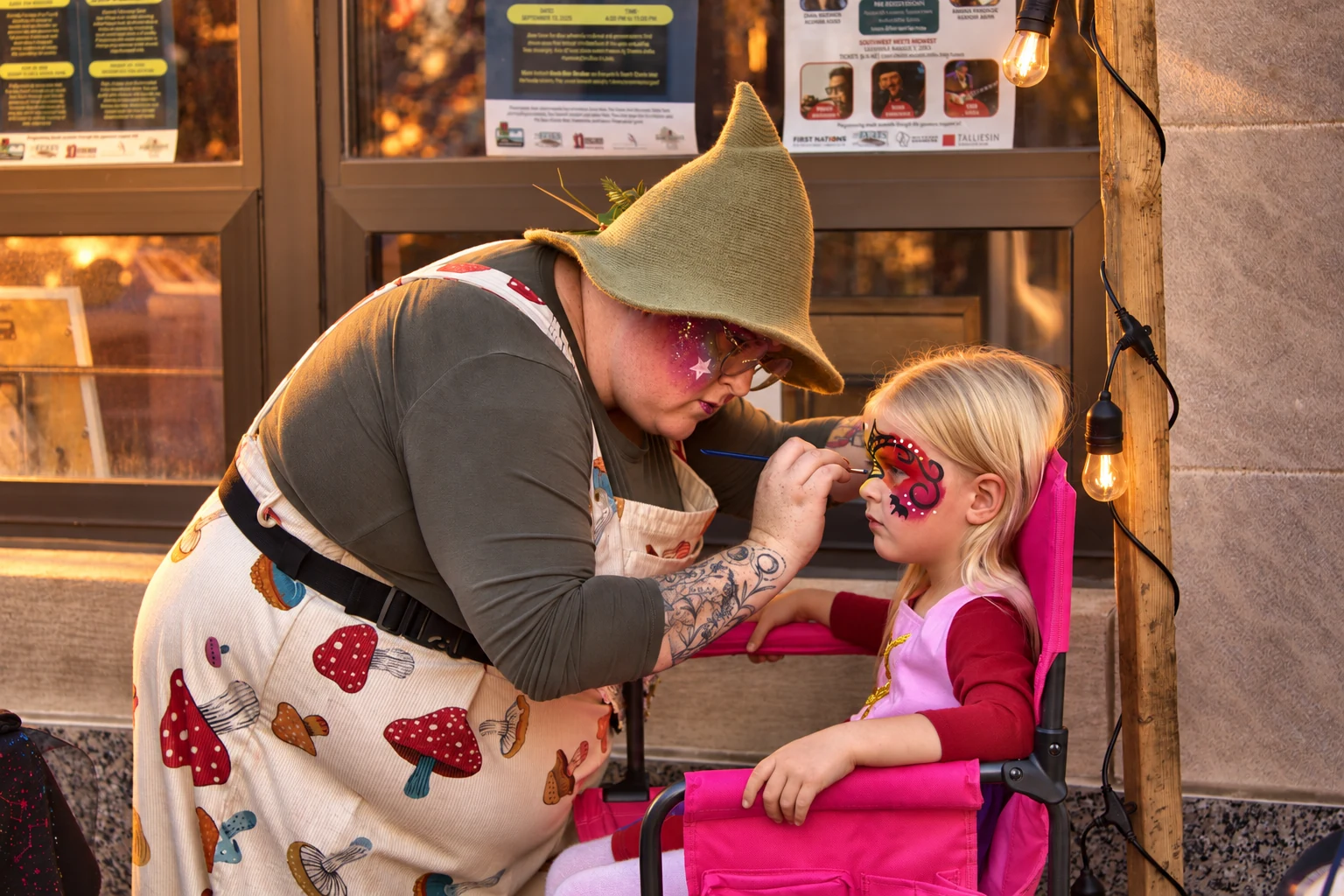 A face painter in a green hat carefully painting a child’s face