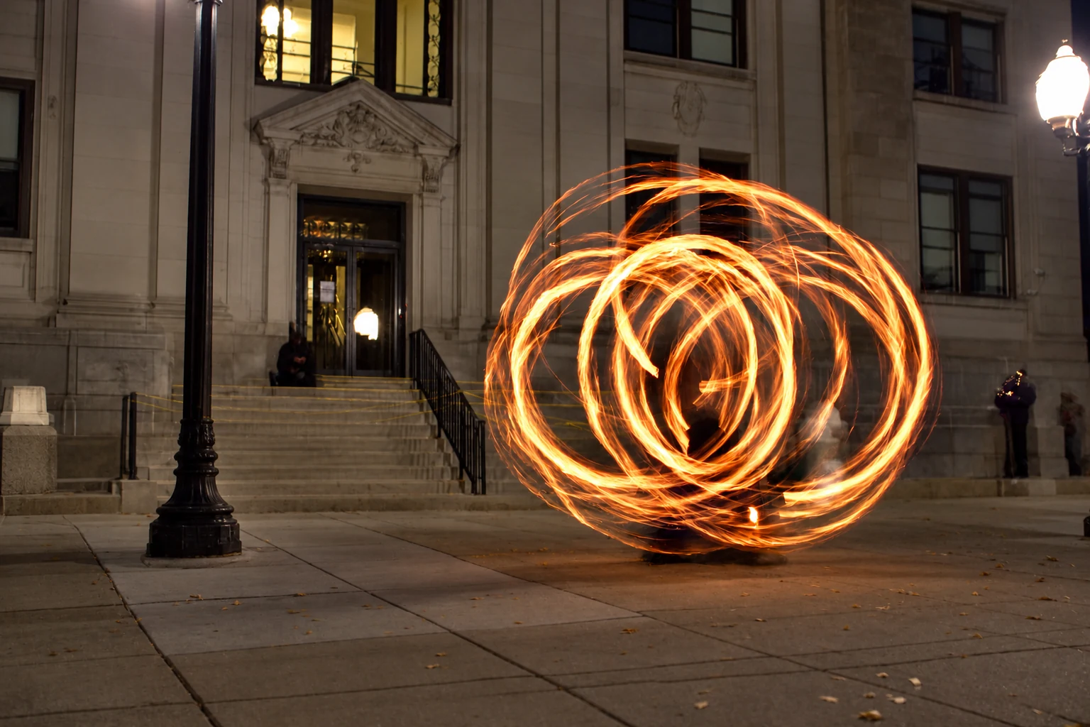 Circles of fire surrounding a performer outside a stone building after dark