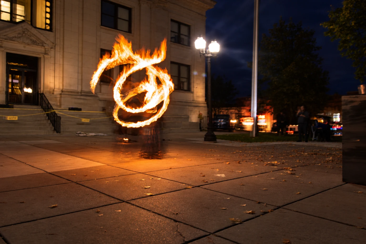 A fire performer tracing bright loops on the sidewalk after dark
