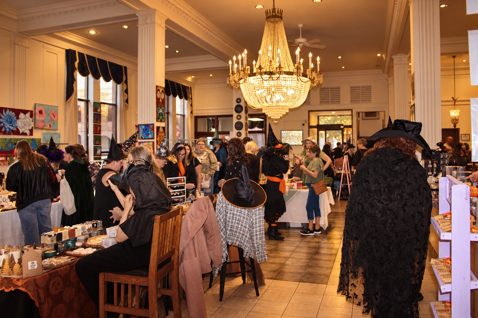 Costumed shoppers and vendors filling a room lined with art and handmade goods