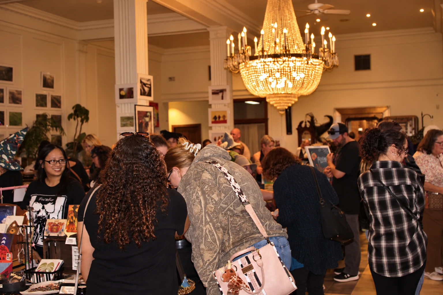 Shoppers browsing indoor vendor tables beneath a glowing chandelier