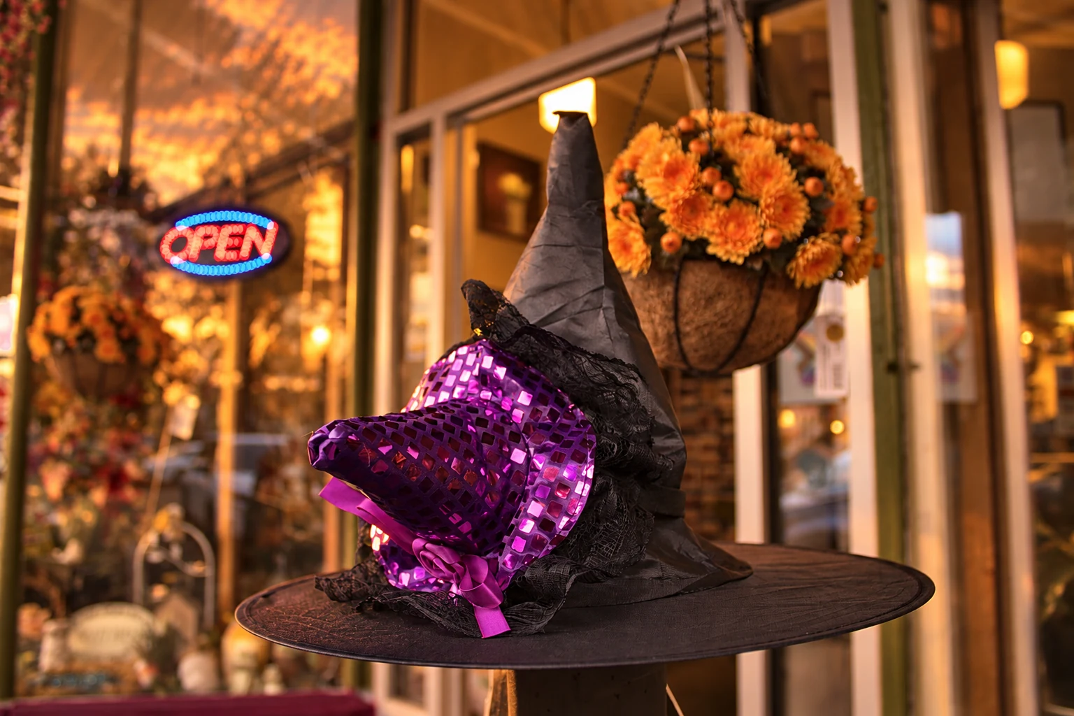 A black witch hat decorated with purple sequins beneath a basket of orange flowers