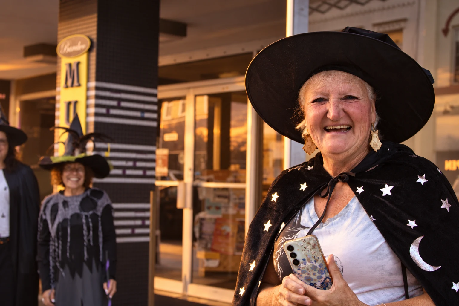A laughing visitor in a black hat and a cape decorated with stars and moons
