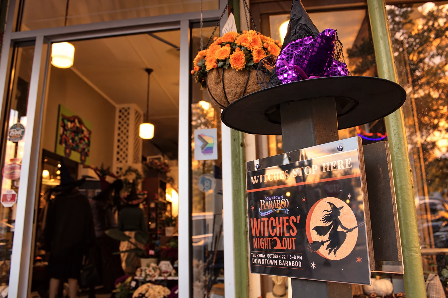 A purple-trimmed witch hat above a Witches’ Night Out poster outside a downtown shop